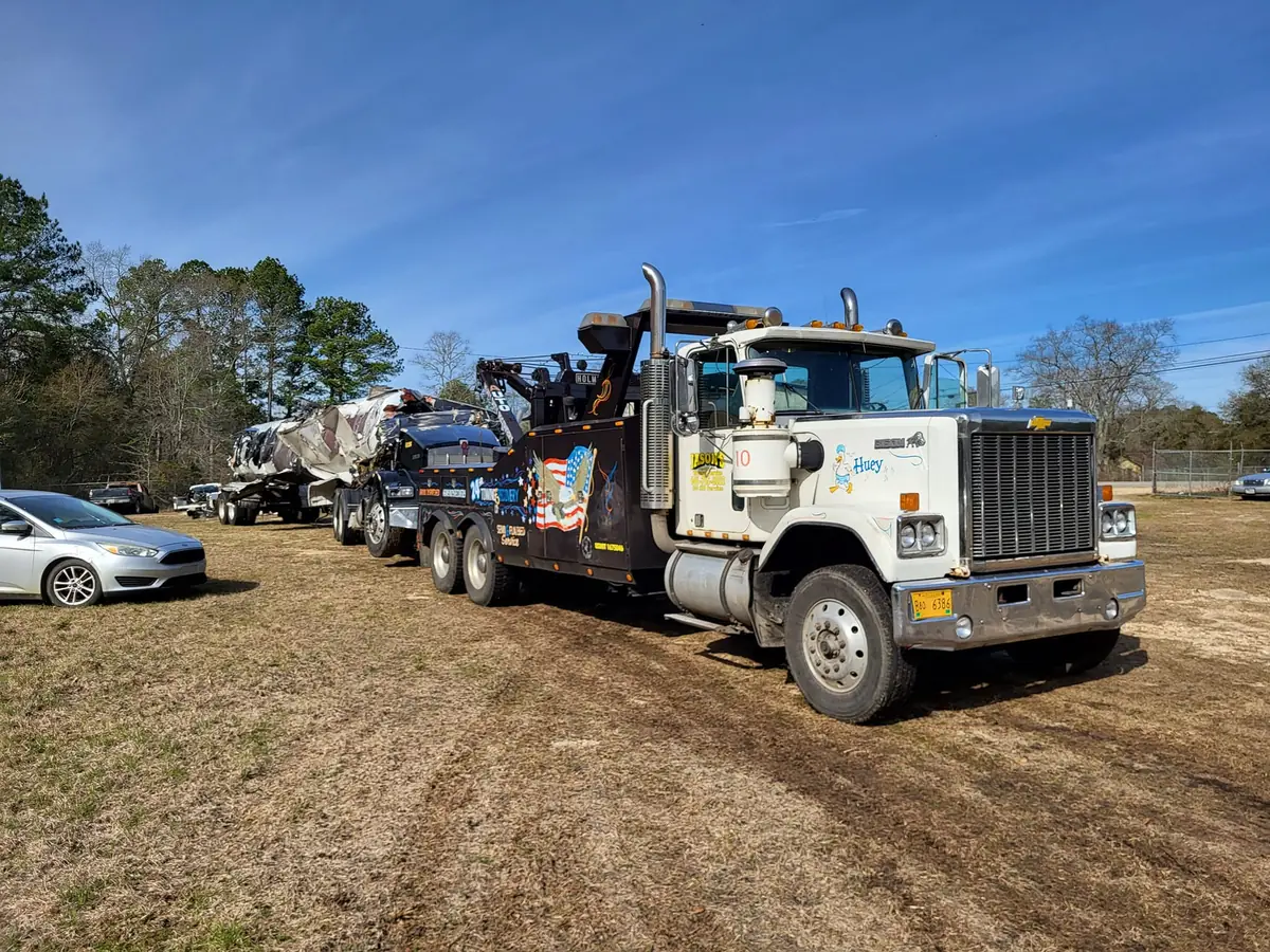 Jason's Wrecker Service's heavy wrecker towing a pickup with a boat on a trailer behind it